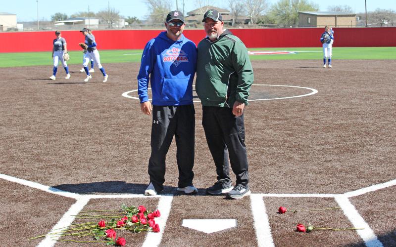 (TC GORDON | THE GRAHAM LEADER) Graham head coach Adam Arrington (left) and former Graham head coach who’s now head coach of Kennedale Philip Irby (right) stand behind home plate with roses in each of the batter’s boxes in tribute of the original Lady Blues softball coach Jimmy Hogan, who passed away a few days before the tournament.