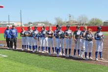 (TC GORDON | THE GRAHAM LEADER) The Lady Blues players and coaches stand with roses in hand as they listen to a tribute to Graham’s first softball coach, Jimmy Hogan, who passed away in the days leading up to this tournament.