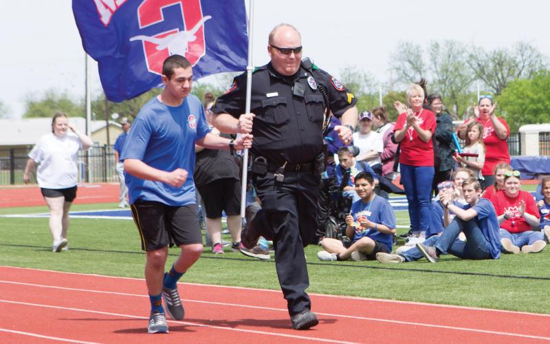 (ARCHIVE PHOTO | THE GRAHAM LEADER) Graham High School Resource Officer Blake Davis runs alongside Tristan Dunlap to begin the Graham Special Teams Track Meet in 2019 at Newton Field.