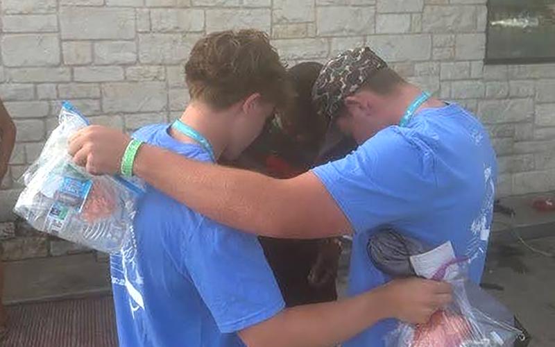 (KENZIE KLINE | CONTRIBUTED PHOTO) Eastside Church of Christ youth pray over a struggling man during an evening street reach. Several volunteers flooded the surrounding area to pray for the homeless and needy. They also handed out bags with food, water, and hygiene as a means of initiating conversation. 