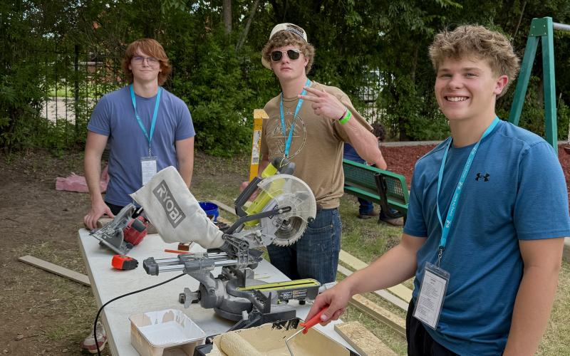 (KENZIE KLINE | CONTRIBUTED PHOTO) Harley Vaughan, Cody Epperson and Cooper Wilde take a break from painting the Men’s Discipleship Home on site of The Feet Ministries to smile for a picture. They, among others, worked throughout the week to paint the outside of the building in order to improve the community facilities. 