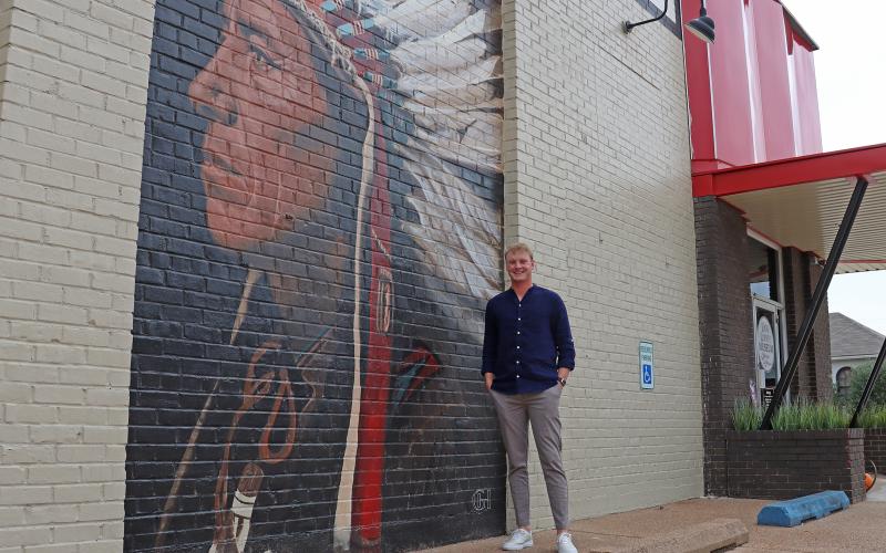 (THOMAS WALLNER | THE GRAHAM LEADER) Local artist Gaven Henderson stands next to a partially completed mural at the Young County Museum of History and Culture. The mural is one of five he will complete for the wall of the museum.