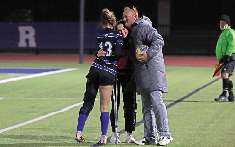 (THOMAS WALLNER | THE GRAHAM LEADER) Head coach Casey Weil and Lady Blues player Tara Dawson hug senior Camden Thorne who was able to make the first play for the team. It was one last moments Thorne could share on her home field with her teammates.