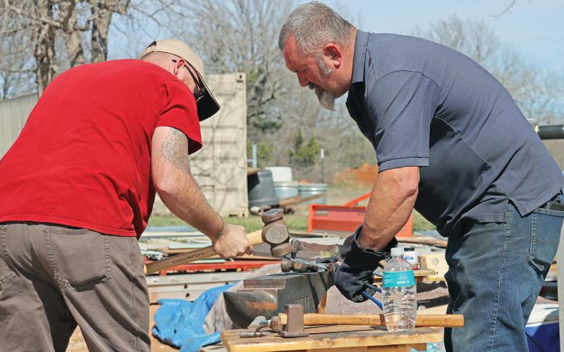 (THOMAS WALLNER | THE GRAHAM LEADER) Instructors Bill Poor (right) and Benjamin Dean hammer a piece of steel on an anvil during an event Saturday, March 2 for veterans and first responders at the home of Greg Coker.