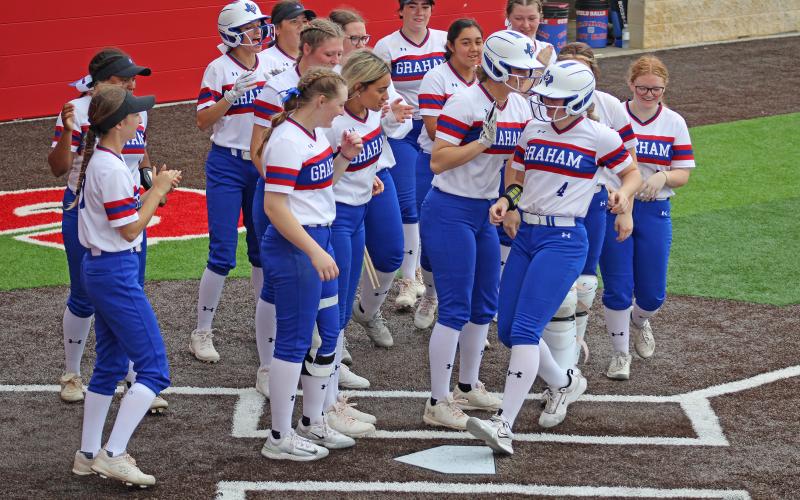 (MIKE WILLIAMS | CONTRIBUTED PHOTO) Mayci Ryans (4) steps on the plate and is greeted by her celebrating teammates after she hit her first home run of the season in Graham’s second game of the bi-district series against Lubbock Estacado. The Lady Blues’ offense powered the team to a bi-district championship.