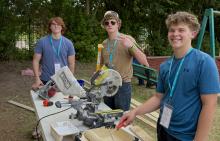 (KENZIE KLINE | CONTRIBUTED PHOTO) Harley Vaughan, Cody Epperson and Cooper Wilde take a break from painting the Men’s Discipleship Home on site of The Feet Ministries to smile for a picture. They, among others, worked throughout the week to paint the outside of the building in order to improve the community facilities. 