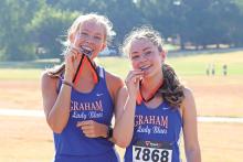 (ARCHIVE PHOTO | THE GRAHAM LEADER) Graham duo of Rebekah Gilbertson (left) and Sonya Clarke (right) bite their silver medals that they received for their second place finish Wednesday, Aug. 21 at the Nocona Relays. 