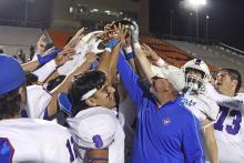 (TC GORDON | THE GRAHAM LEADER) Graham head coach Clay McChristian and his players lift the bi-district championship trophy above their heads Thursday, Nov. 14 following their 60-0 crushing of the Dunbar Wildcats.